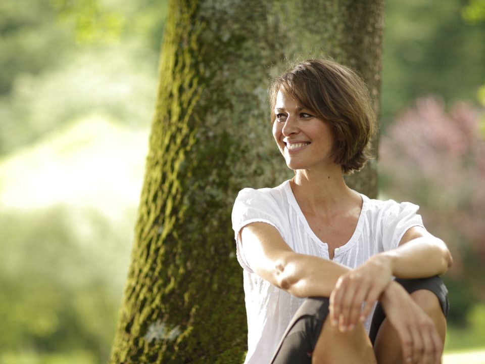 gesundes-bayern-frau-laechelnd-entspannt-am-baum-sitzend